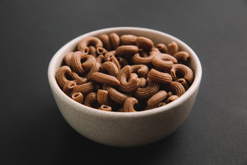 Whole grain elbow macaroni on dark background, close up