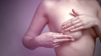 Naked young woman due to pain conducts an independent examination of the breast to preserve women's health. Soft focus, tint and copy space