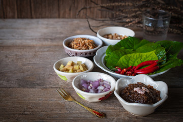 Miang kham,A royal leaf wrap appetizer Consist of Shallot, Ginger, Fried beans, Slice of lemon, Betel leaf, Chilli, Fried coconut and chili sauce, whole placed on the wood table.