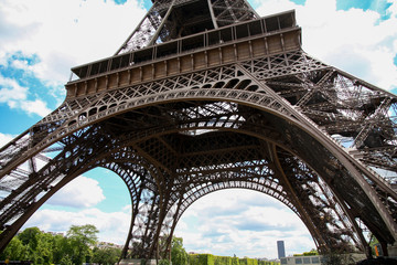 Low angle shot of the base of iconic Eiffel Tower on a spring summer day with blue sky and white clouds. Tourists consider Paris as the world's most romantic city and Eiffel tower most visited place 