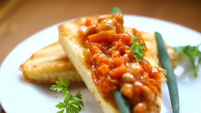 fried bread toasts with stewed beans and vegetables in a plate on a wooden table