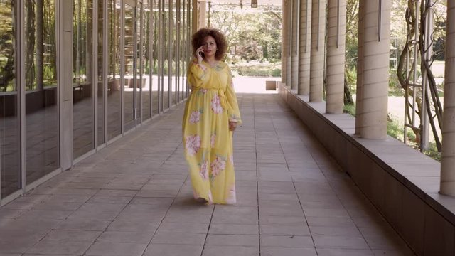Eine attraktive Frau im gelben Kleid telefoniert im Park