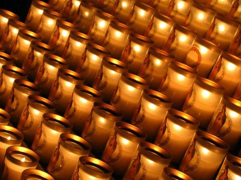 Diagonally shot photos of lit up candles with image of Saint Maria at the Notre Dame Cathedral, Paris, France arranged and displayed in rows at the church before fire hazard