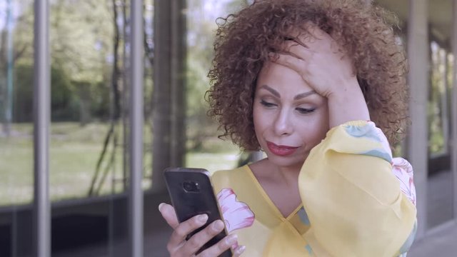 Eine Frau checkt Nachrichten auf Ihrem Mobiltelefon und schaut mit unterschiedlichen Gesichtsausdr&uuml;ck