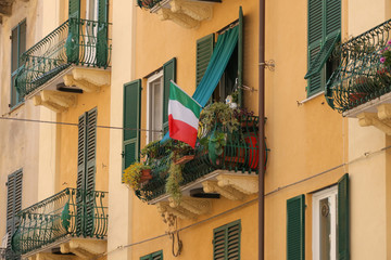 Fototapeta na wymiar Balcony with flowers and Italian flag, house facade, Italy