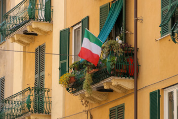 Balcony with flowers and Italian flag, house facade, Italy