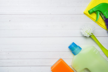 Bottles with detergents, brushes and sponges on wooden background. Colorful cleaning products. Home cleaning concept. Top view, copy space.