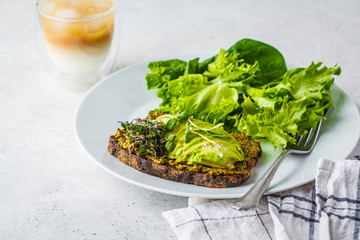 Avocado toast with pesto, sprouts and salad on white plate.