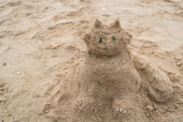 Funny sand sculpture of a cat on the beach. Summer holidays