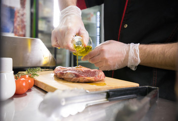 Restaurant kitchen. A chef preparing a of meat raw piece of meat and pouring an oil on it