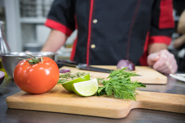 Restaurant kitchen. A tomato and lime on the desk on the foreground. Chef standing on the background