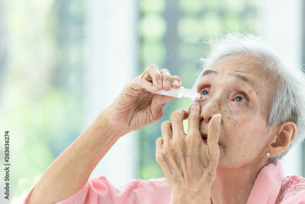 Wall mural asian senior woman putting eye drop,closeup view of elderly person using bottle of eyedrops in her e