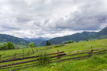 Fototapeta na wymiar Mountain slope with fenced hayfields on a foreground