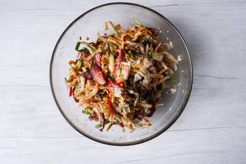 Asian food dish salad with meat and fried in wok vegetables. White background, top flat view.
