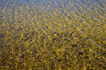 Transparent water surface with ripples through which the sandy bottom with pebbles is visible
