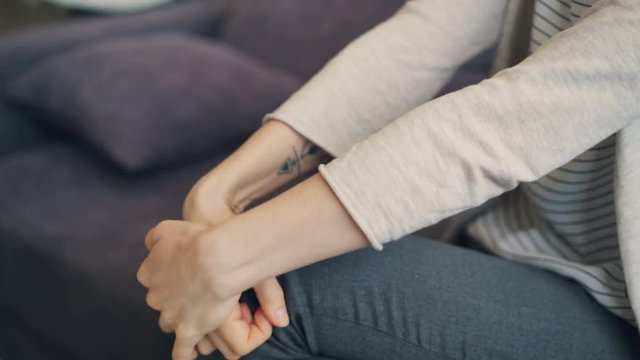 Close-up shot of anxious young woman's hands moving during session with therapist. Girl is sitting on couch in office and clenching palms with anxiety.
