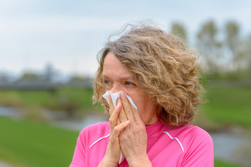 Woman outdoors blowing nose in napkin