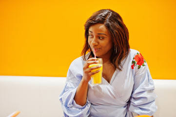 African woman sitting on cafe against orange wall drink pineapple juice in hands.