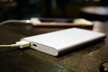 Powerbank charging smartphone on wooden background close up view