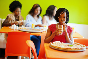 African woman with pizza sitting at restaurant and drink juice against dark skinned girls.