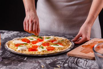 Obraz na płótnie Canvas young woman in a gray aprong prepares a pizza margarita