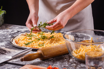 young woman in a gray aprong prepares a vegetarian pizza