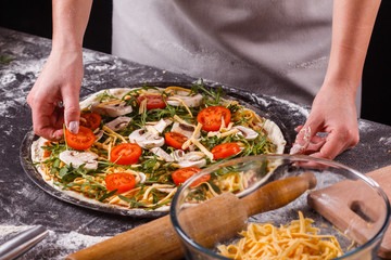 young woman in a gray aprong prepares a vegetarian pizza