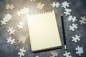 Top View of jigsaw puzzle and blank notebook with pencil on black background. Business solve problem concept.