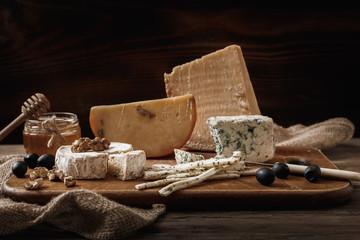 Different types of cheeses. slices of cheese brie or camembert with parmesan, cheddar ,blue cheese , and other with nut and honey on wooden board on dark background