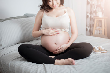 Beautiful asian pregnant woman sit on bed and touching her belly
