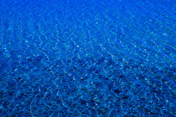Blue water surface with ripples through which the sandy bottom with pebbles is visible