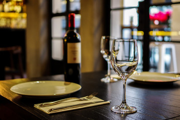 Empty wine glasses and a bottle of wine. Empty white plate with fork and knife on  wooden table close to window