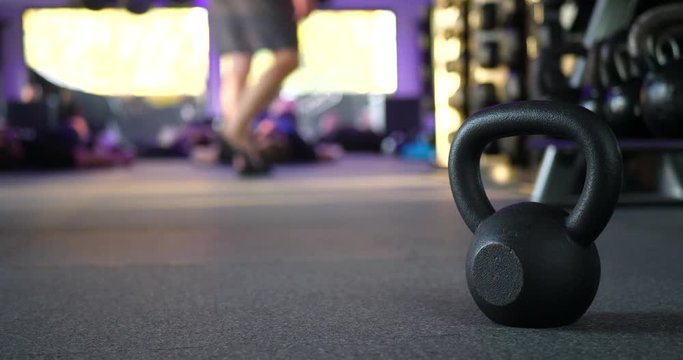 A kettlebell weight in a gym with people working out in a fitness training class in the background.