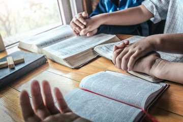 Children group holding hands with praying together around table at home, prayer meeting concept.