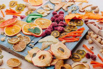 Mixed dried fruit and vegetable chips, candied pumpkin slices, nuts and seeds on blue wooden board