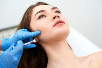 Beautician doctor with filler syringe making injection to jowls. Masseter lines reduction and face...