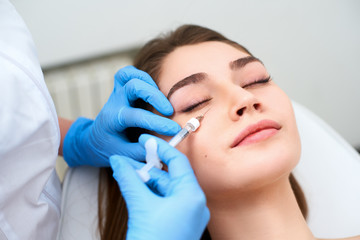 Doctor in medical gloves with syringe injects botulinum under eyes for rejuvenating wrinkle...