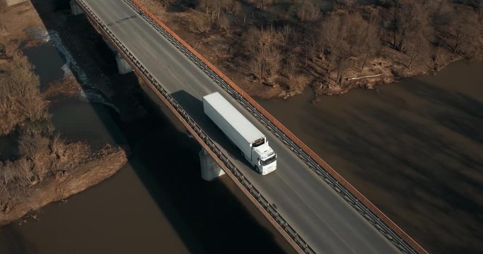 Truck driving / traveling on highway and bridge through the river aerial footage at spring time / top view / Highway truck traffic