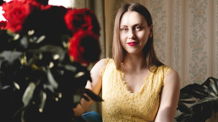 Naklejka premium Nice romantic sweet woman with bouquet of red roses in beige interior apartment. Concept of tenderness and womans feeling. Saint Valentines day.