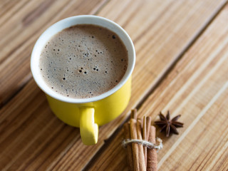 Yellow cappuccino coffee mug on wooden background with cinnamon