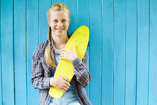 Fashion girl. Stylish teenager wearing a summer jeans clothes,  with skateboard having fun in city over colorful blue background