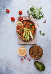 healthy vegetarian salad with roasted pumpkin, chickpea, tomatoes, pumpkin and sunflower seeds, garlic and green herbs, avocado and spices on gray background, top view, copy space