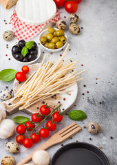 Homemade spaghetti pasta with quail eggs with bottle of tomato sauce and cheese on kitchen background. Classic italian village food. Garlic, champignons, black and green olives, pan and spatula.