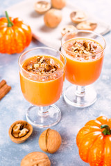 Healthy pumpkin smoothie with walnuts and cinnamon in glasses on rustic background