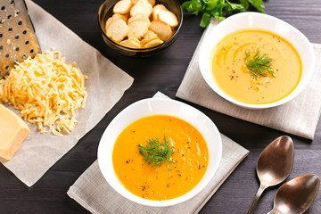Pumpkin cream soup with croutons and fresh dill and parsley on dark wooden background, top view