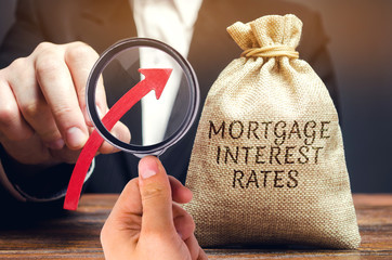Bag with the money and the word Mortgage interest rates and up arrow in male hands. Raising...