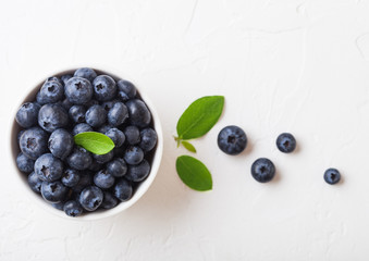 Fresh raw organic blueberries with leaf in white china bowl on white background. Top view. Space for text