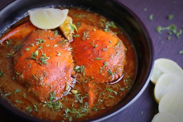 Indian Cuisine, Spicy Crabs Curry in red gravy, garnished with fresh coriander and lemon wedges or lemon slices on dark moody background
