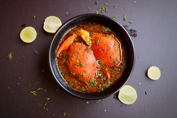 Indian Cuisine, Spicy Crabs Curry in red gravy, garnished with fresh coriander and lemon wedges or lemon slices on dark moody background
