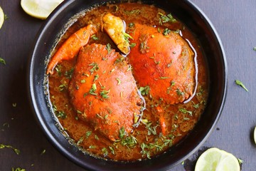 Indian Cuisine, Spicy Crabs Curry in red gravy, garnished with fresh coriander and lemon wedges or lemon slices on dark moody background